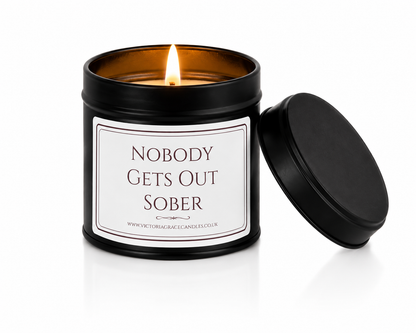 A black metal candle tin with a lit flame, featuring a white label that reads 'NOBODY GETS OUT SOBER' 